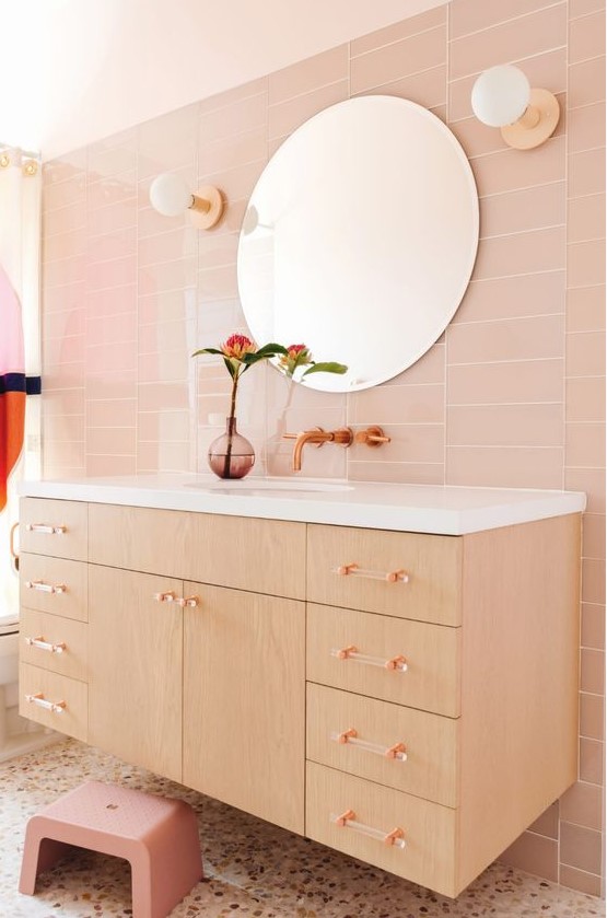 a blush bathroom with skinny tiles, a stained floating vanity, clear glass handles, a pink stool and a terrazzo floor