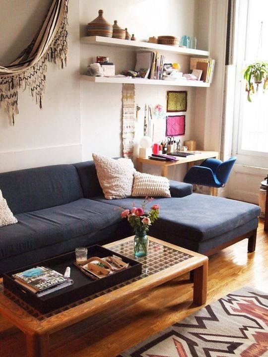 a boho living room with a small desk and shelves at the window, a navy sofa, a coffee table, some boho decor and textiles