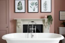 a chic pink bathroom with a non-working fireplace, a white clawfoot tub, a gallery wlal and some greenery