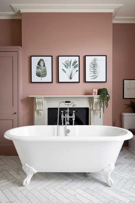 a chic pink bathroom with a non-working fireplace, a white clawfoot tub, a gallery wlal and some greenery