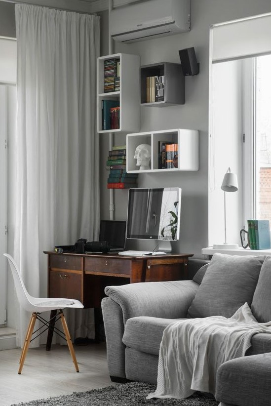 A contemporary grey living room with comfy furniture, a vintage desk and wall mounted shelves on the wall plus a chair