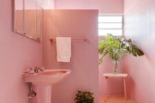 a light pink bathroom clad with square tiles, a free-standing sink, a shower space, a mirror with lights and potted greenery