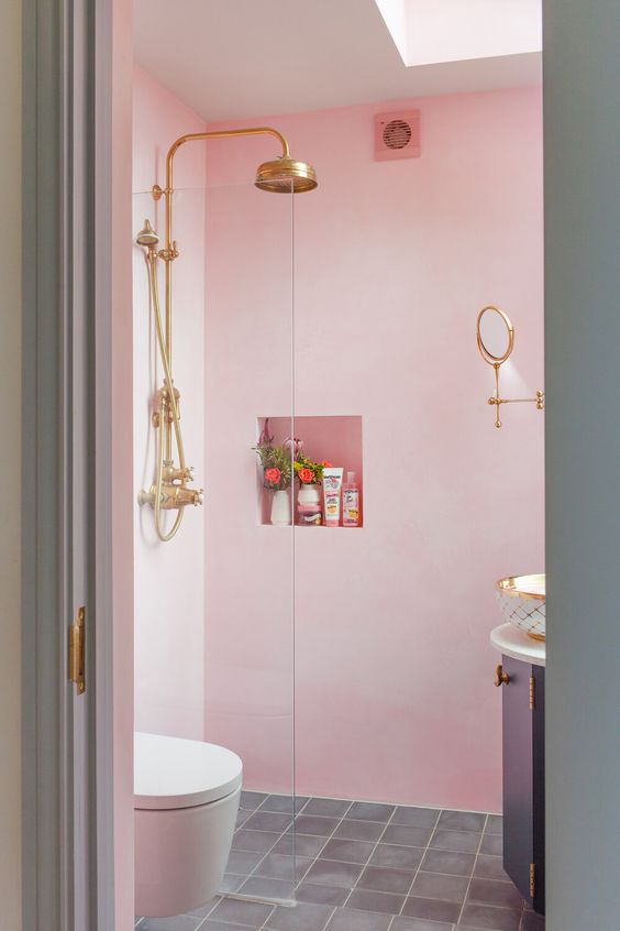 a light pink bathroom with a rounded vanity, a niche shelf, some gold fixtures is a pretty and fun idea, and a skylight adds natural light