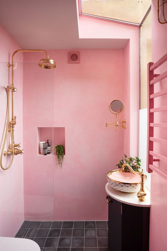 a light pink bathroom with a shower space, a niche shelf, a black vanity with a bowl sink and gold fixtures