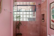 a light pink bathroom with coral tiles in the shower, a window and white appliances and greenery is cool and bright