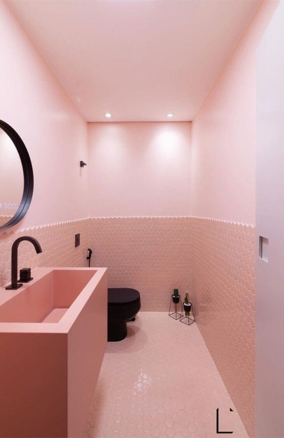 a lovely blush powder room with light pink walls and hex tiles, a pink vanity with a bilt-in sink and black fixtures for a contrast