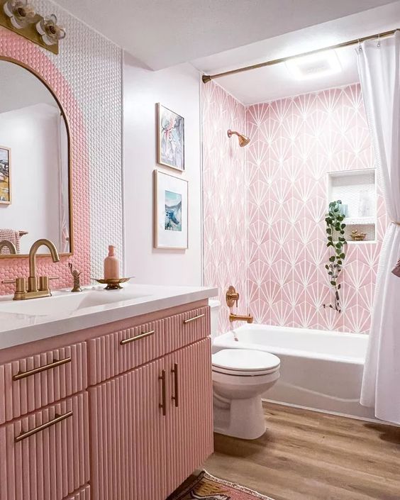 a lovely pink bathroom with printed tiles, pink and white penny tiles, a pink fluted vanity, brass fixtures and potted greenery