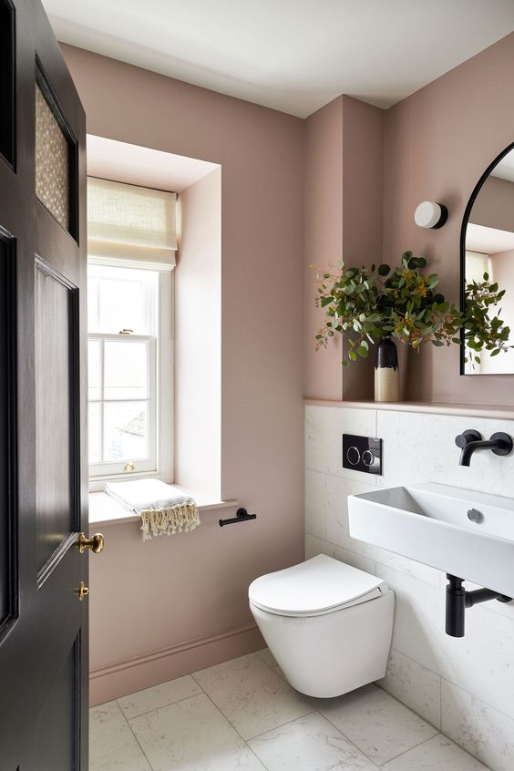 a mauve and white bathroom with white appliances, black fixtures and greenery is amazing for a modern home
