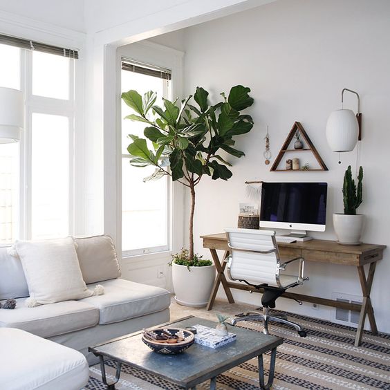 a neutral boho living room with a white corner sofa and neutral pillows, a coffee table, a trestle desk and a white chair, some potted plants