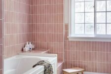 a pastel pink bathroom with skinny tiles, a bathtub and several built-in shelves, a blush curtain and a boho rug