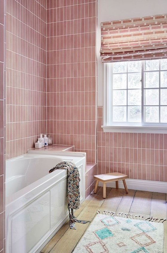 A pastel pink bathroom with skinny tiles, a bathtub and several built in shelves, a blush curtain and a boho rug
