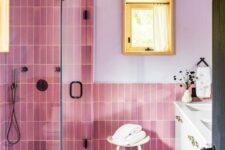 a pink and lilac bathroom with lilac walls, pink skinny and leafy tiles, a white vanity and black fixtures