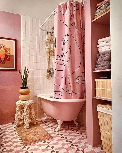 A pink and white bathroom with a pink free standing tub, a printed curtain, geo tiles on the floor and some decor