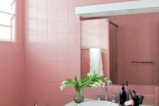 a pink bathroom clad with square tiles, a concrete vanity for a contrast, a mirror with a lamp and a bathtub is lovely