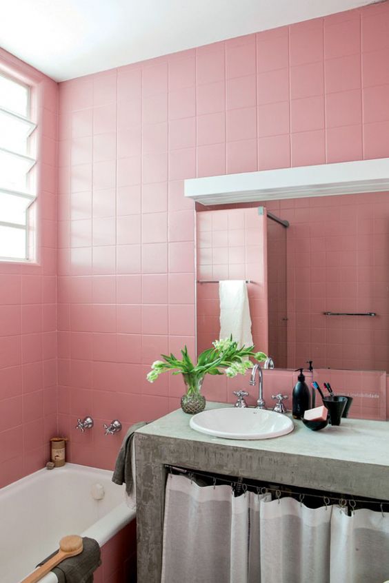 a pink bathroom clad with square tiles, a concrete vanity for a contrast, a mirror with a lamp and a bathtub is lovely