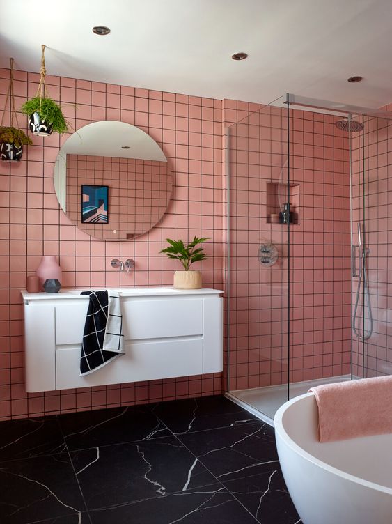 a pink bathroom with a black marble floor, white appliances and a floating vanity, potted greenery and a round mirror