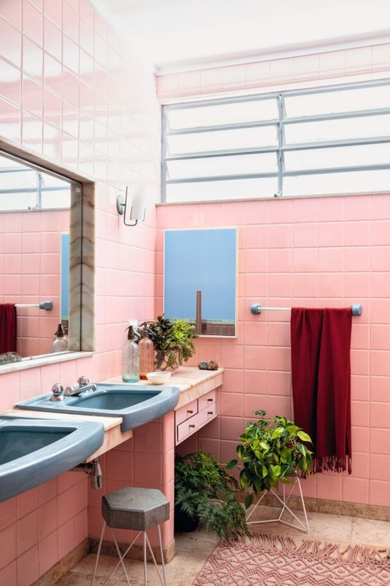 a pink bathroom with a tiled vanity and blue sinks, mirrors, potted plants and a pink boho rug is amazing