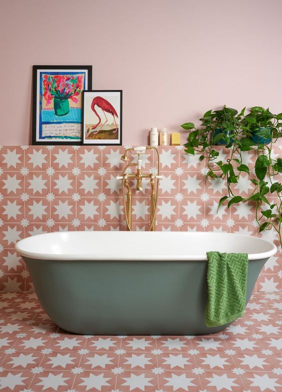 A pink bathroom with light pink walls, beautiful star printed tiles, a green tub, some decor and potted greenery