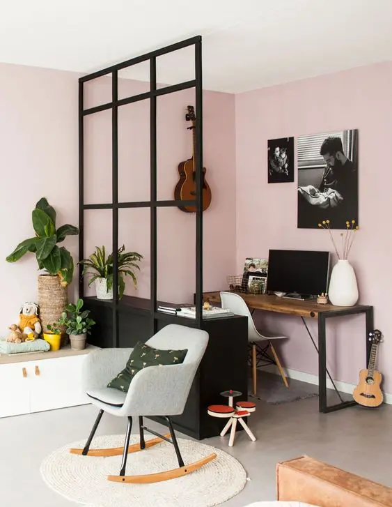 a pink living room with a small working space in the corner, a white chair, some decor and vases, a space divider and some chairs