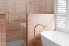 a pretty bathroom with pink and white square tiles, a shower space, an oval tub and gold fixtures is lovely