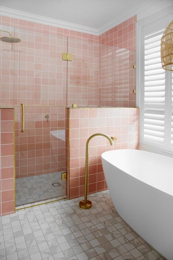 a pretty bathroom with pink and white square tiles, a shower space, an oval tub and gold fixtures is lovely