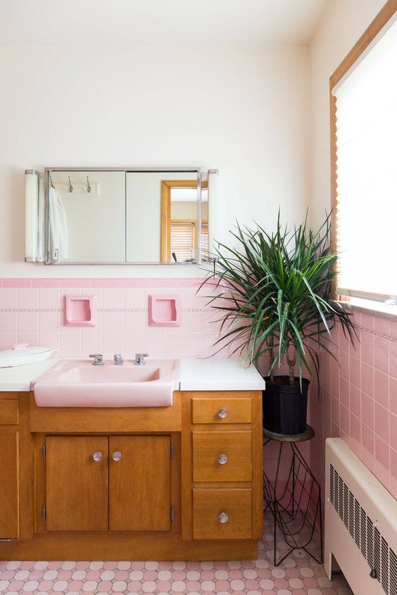 a pretty mid-century modern bathroom with light pink and printed pink tiles, a stained vanity, a mirror cabinet and a potted plant