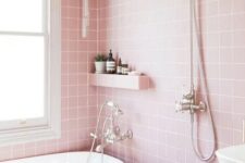 a pretty pink bathroom clad with square tiles, a white tub and a sink, a built-in shelf and a vanity plus lights
