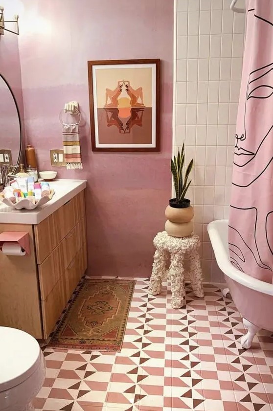 A quirky pink bathroom with geo tiles on the floor, a pink free standing bathtub and a pink curtain, a light stained vanity