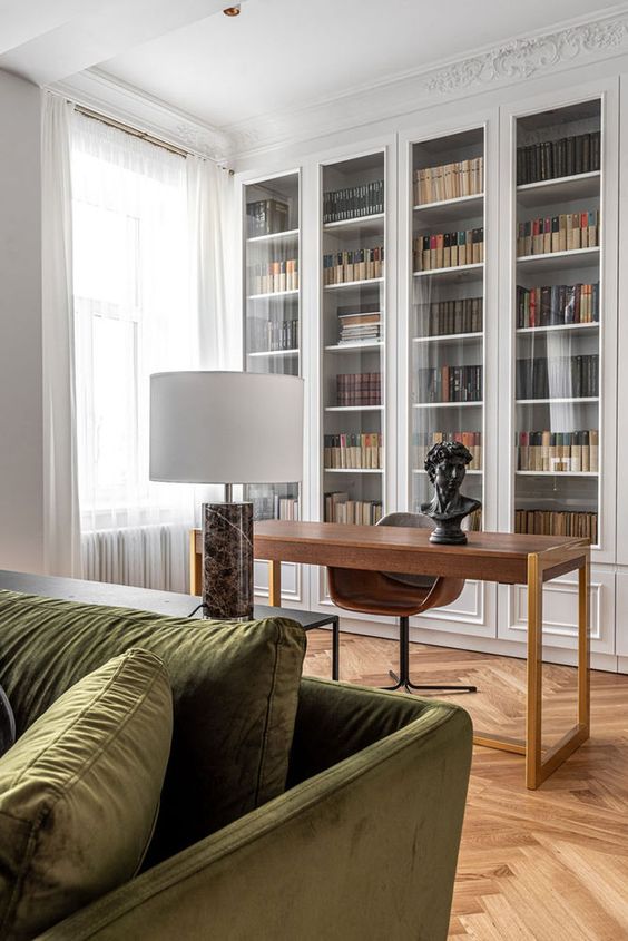 a refined living room with built-in bookcases, a stained desk and a chair, a black coffee table and green velvet sofa