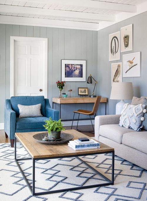 a seaside living room with light grey walls, a desk, a blue chair, a neutral sofa and pastel pillows, a coffee table and artwork