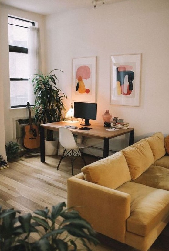 a welcoming living room with a yellow sofa, a working space by the window, a pretty gallery wall and potted plants is cozy