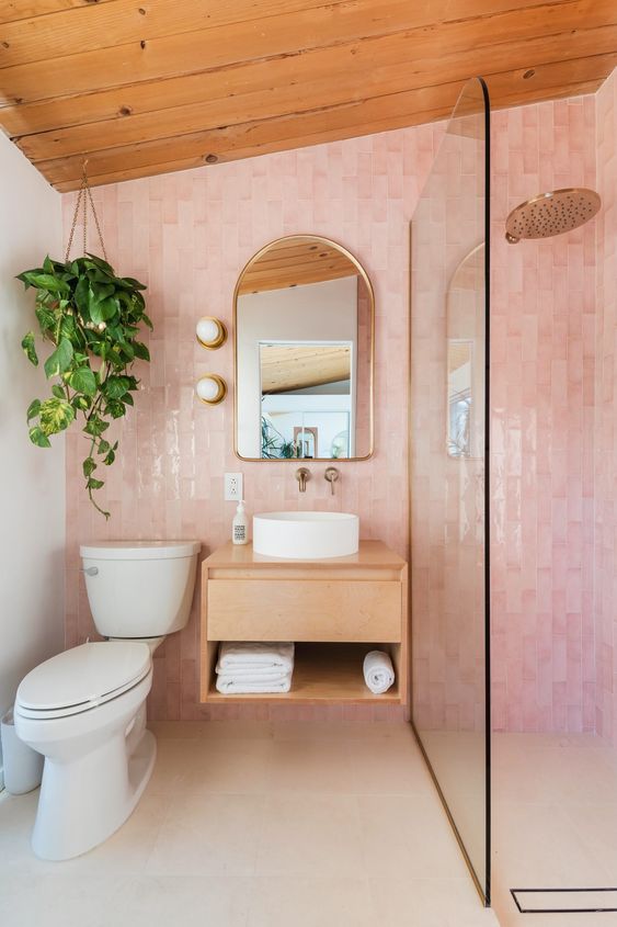 an attic bathroom with a blush tile accent wall, a shower space, a floating vanity, an arched mirror and a potted plant
