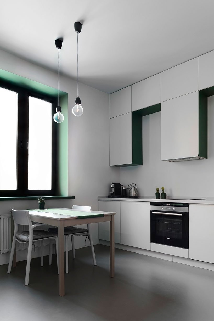 The kitchen is done with sleek white cabinets, a simple table and chairs and toiches of emerald here and there, plus there are two pendant lamps over the table
