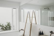 02 a minimalist white bathroom with a long mirror, a free-standing bathtub, a stone sink and a ladder for storage
