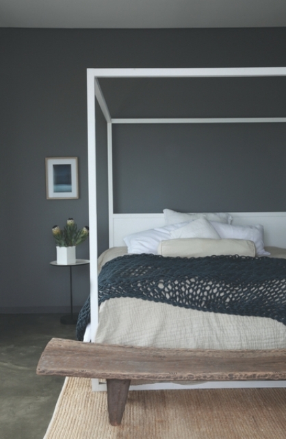 A guest bedroom is done with a graphite grey statement wall, a wooden bench and a framed bed plus textiles