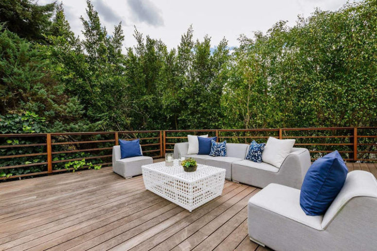 The deck features comfy upholstered furniture and there's lush greenery all arond the space