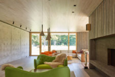 04 The living room is done with a large fireplace clad with brick and wood and a couple of bold green sofas