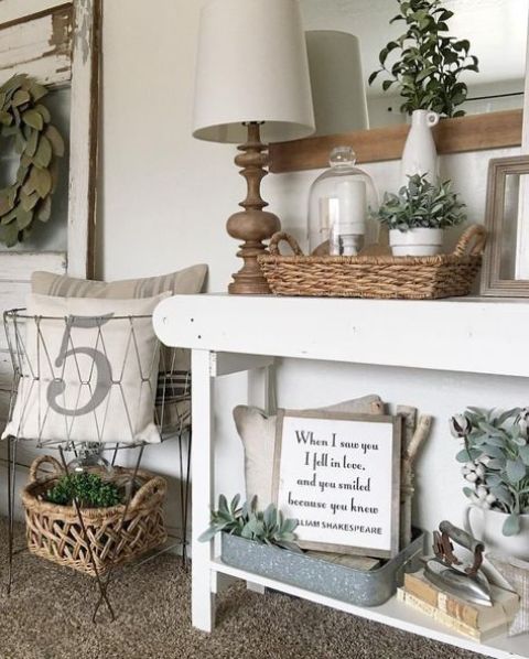 a farmhouse console table with a basket, much greenery in vases and some antique finds