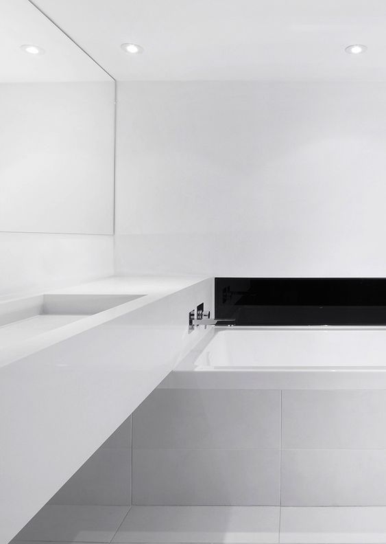 An ultra minimalist white bathroom with a black built in fireplace and a long vanity