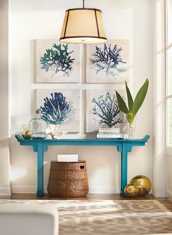 a turquoise console with a gallery wall of coral artworks, bottles and a basket