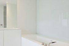 06 a minimalist white bathroom with a covered bathtub, a large mirror and a vanity