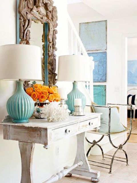 a whitewashed console table, a coral, turquoise lamps and a mirror clad with driftwood