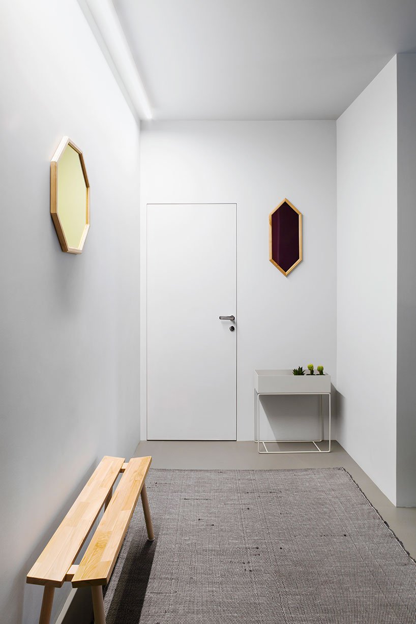 The entryway is done in white, with geometric mirrors and a textural rug plus a planter