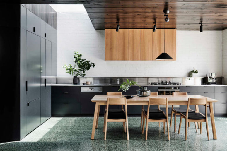 The kitchen features sleek black cabinets, upper light-colored wooden ones and some potted greenery
