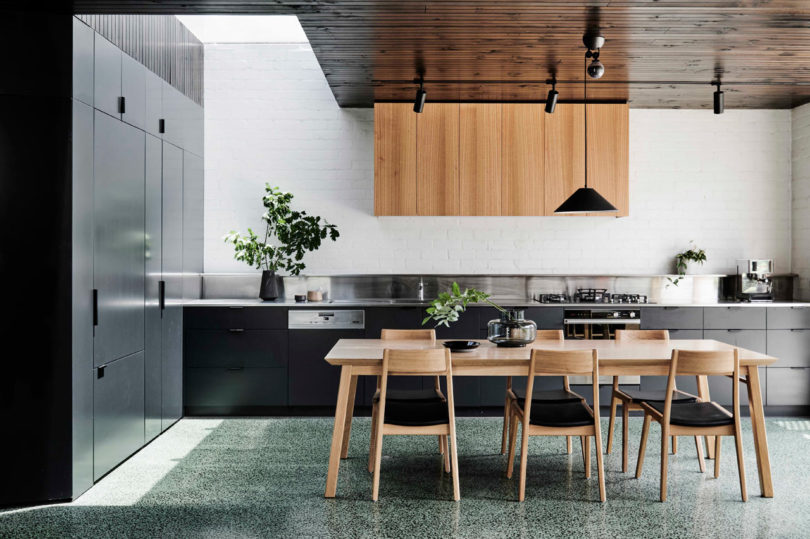 The kitchen features sleek black cabinets, upper light colored wooden ones and some potted greenery