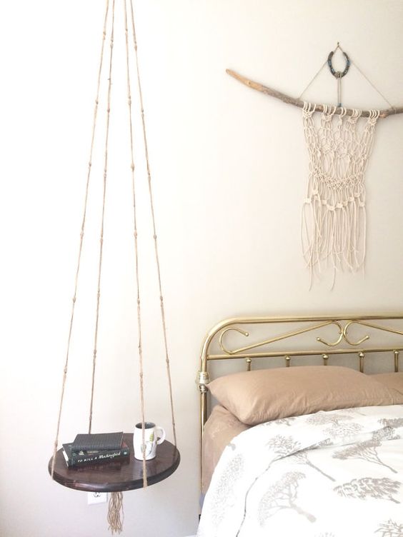 a boho bedroom with a hanging bedside table of dark stained wood and yarn that makes the space even more boho