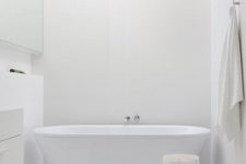 07 a chic white bathroom with a free-standing bathtub, a whitewashed stool and minimalist furniture