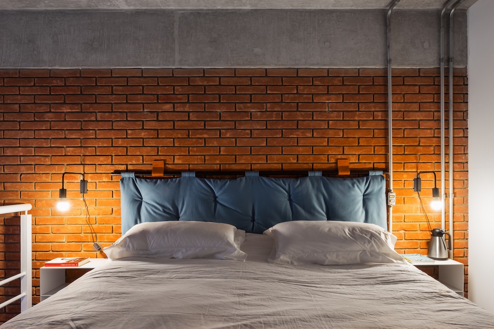 The bedroom has a large comfy bed with a blue upholstered headboard and industrial sconces