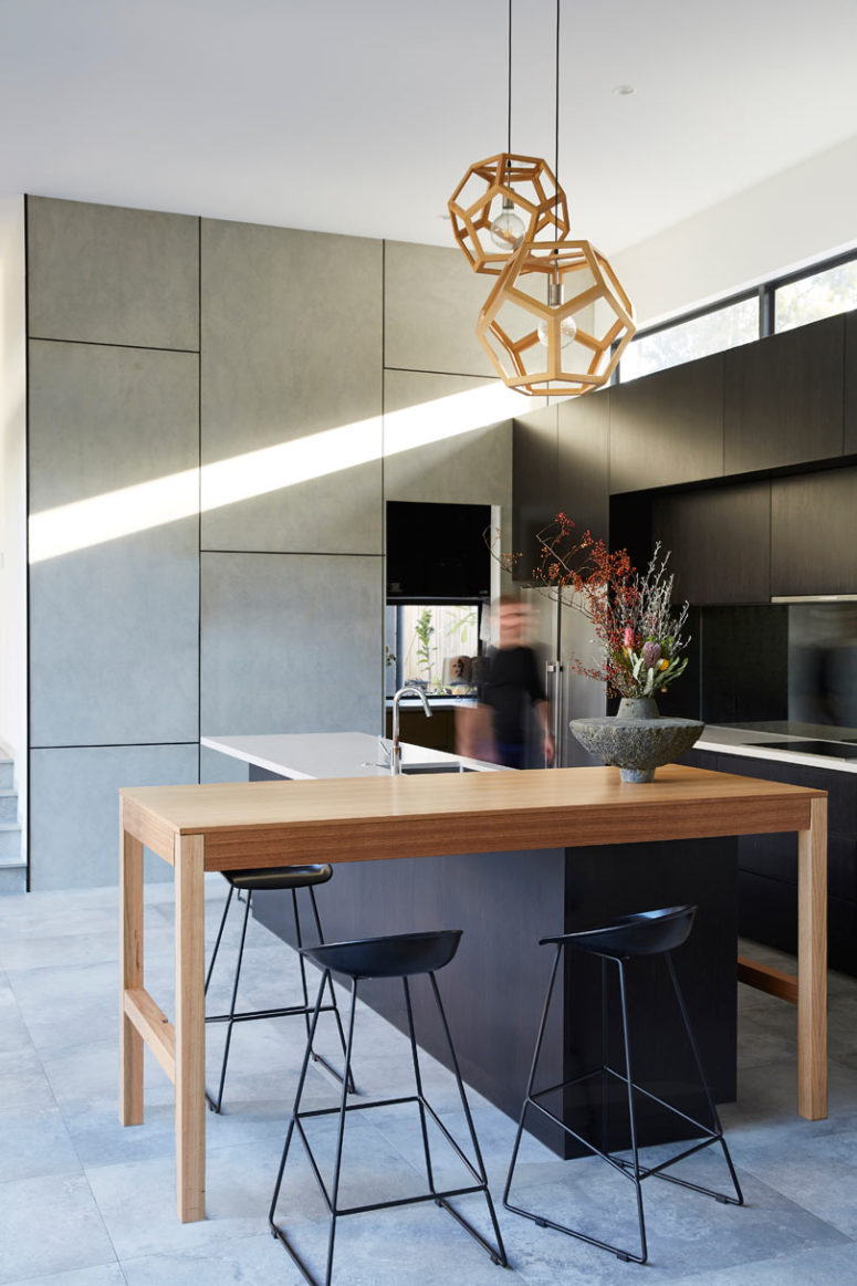 The kitchen is done with sleek grey and black cabinets, a wooden console table for having a meal and a kitchen island