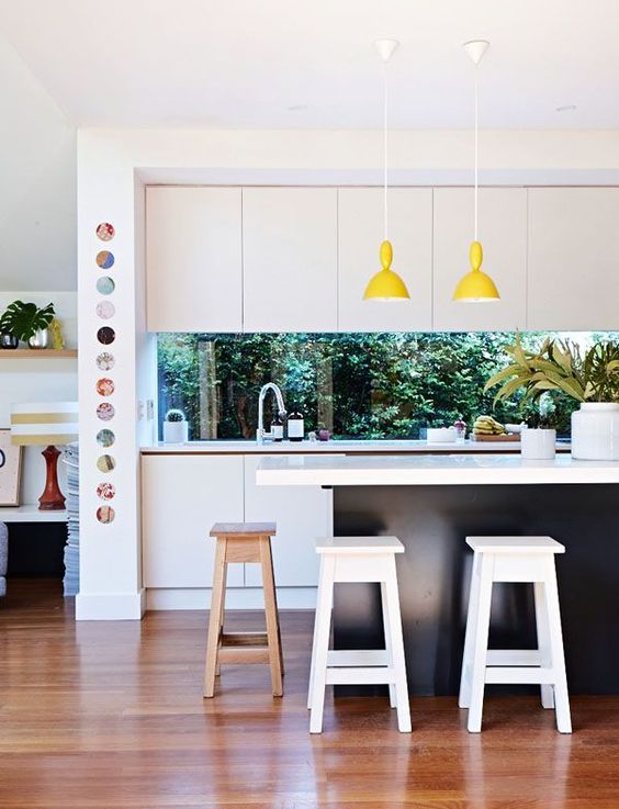 a contemporary black and white kitchen is spruced up with yellow lamps and a window backsplash